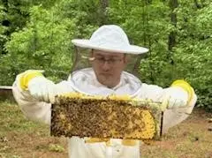 Anthony in Beekeeper suit holding up a bee frame